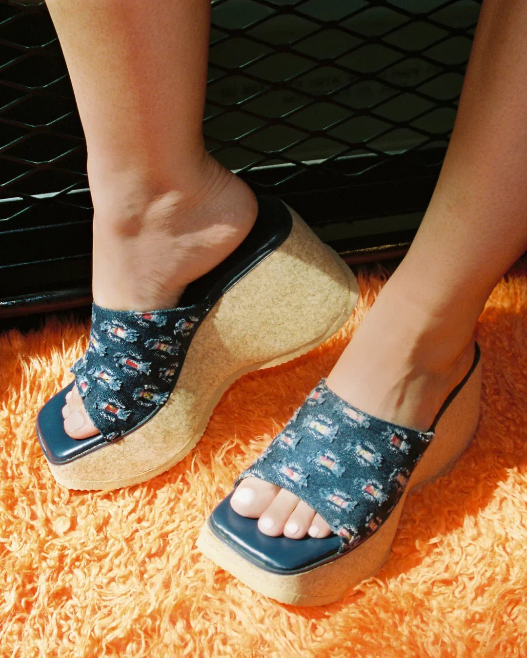 Woman wearing open-toe denim platform slide sandals with cork soles on orange carpet