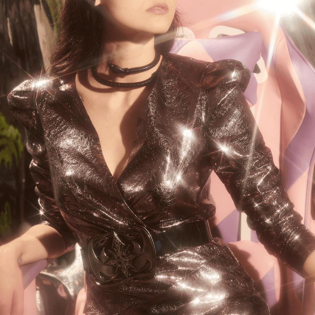 Woman wearing metallic long sleeve dress with black belt and choker, seated indoors