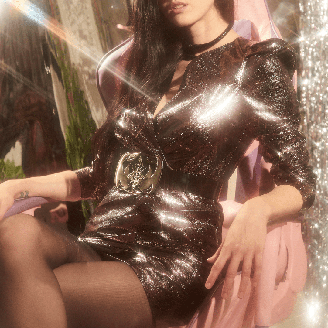 Woman in a shiny metallic dress with black tights, wide belt, and puffy sleeves, seated