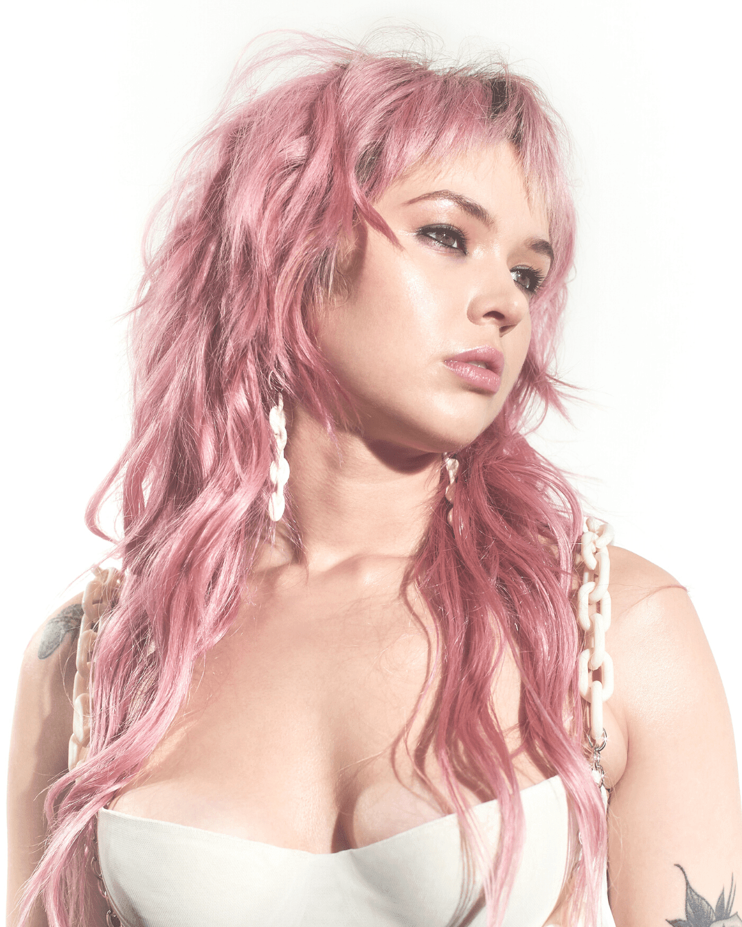 Woman with pink hair wearing white chain earrings and matching chain strap top