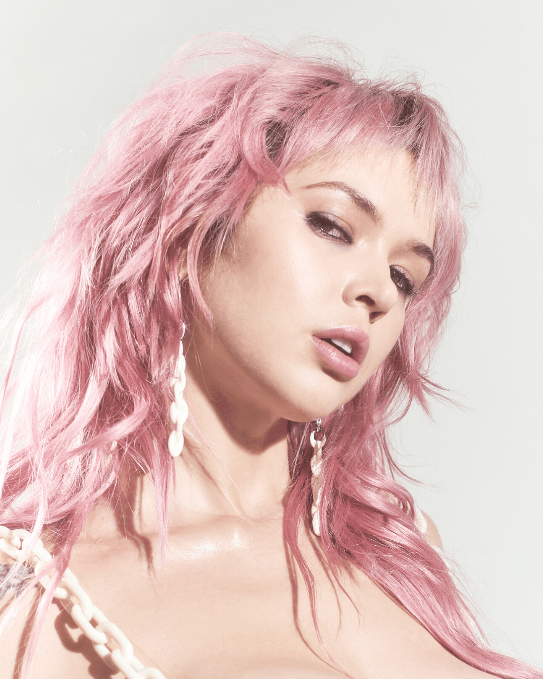 Woman with pink hair wearing long white chain-style earrings and matching necklace