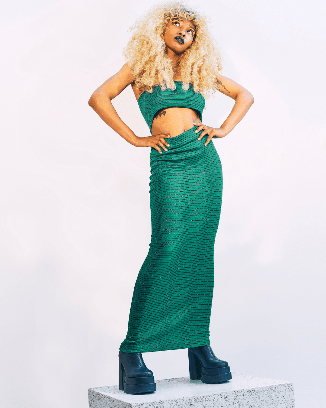 Woman wearing a green knit crop top and matching long skirt with black platform boots