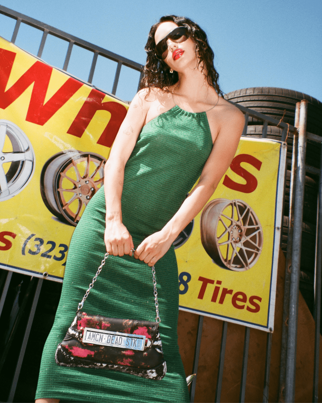 Woman in a sleeveless green ribbed dress holding a black chain-strap handbag outdoors