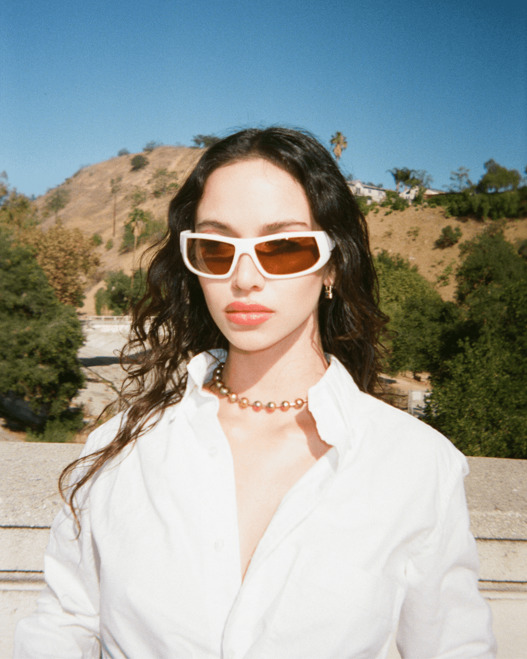 Woman wearing a white button-up shirt and white sunglasses outdoors in sunlight