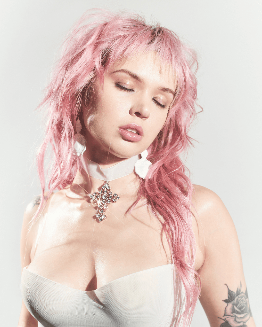 Woman with pink hair wearing white choker with jeweled cross pendant and white strapless top