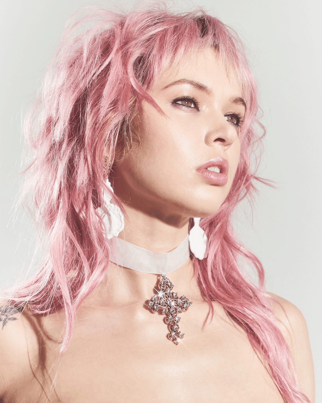Woman with pink hair wearing a white choker necklace with a large jeweled cross pendant