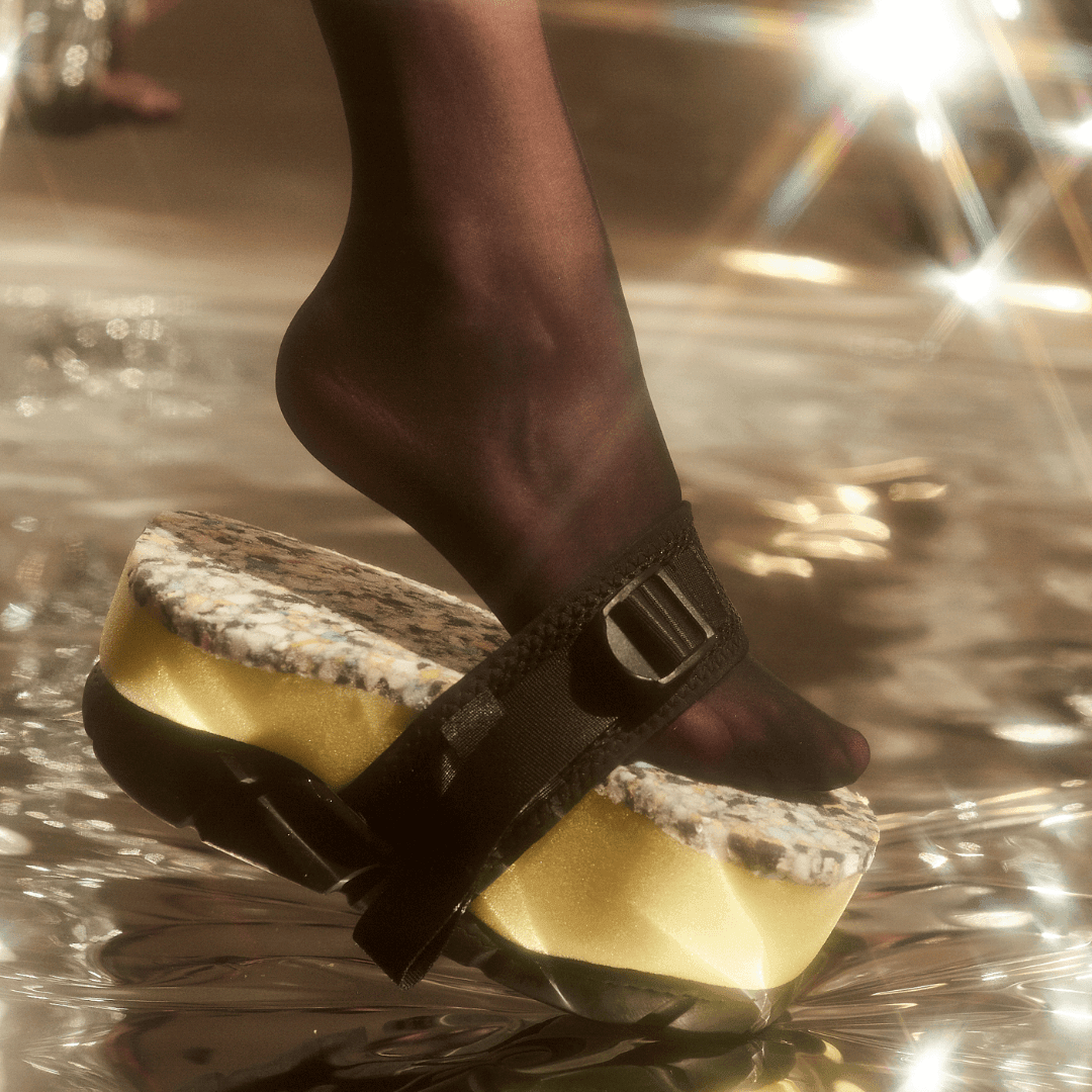 Black strap platform sandal with speckled sole and gold midsole, worn with black tights