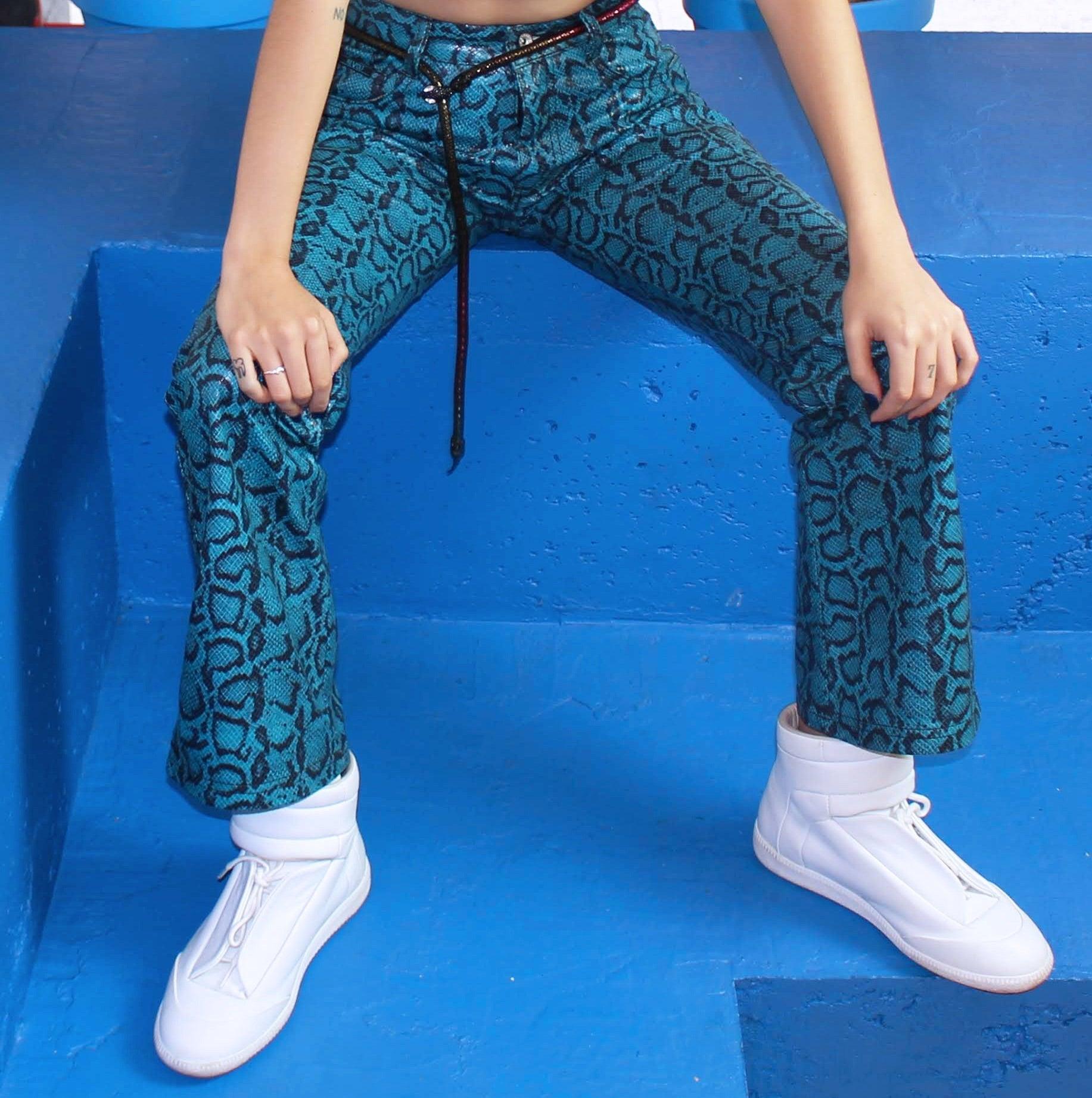 Person wearing blue snake print pants and white sneakers sitting on a blue surface