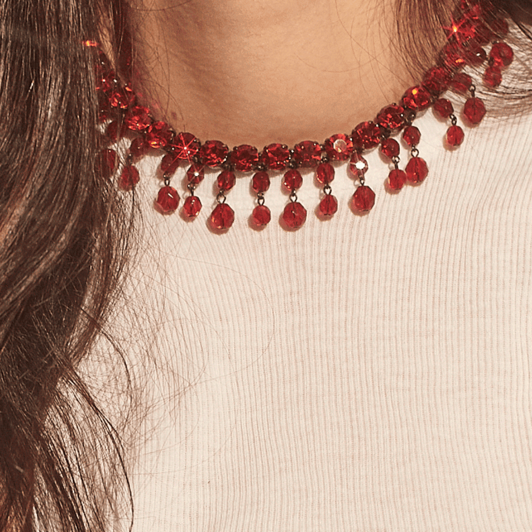 Red beaded choker necklace with dangling beads on a person wearing a white top
