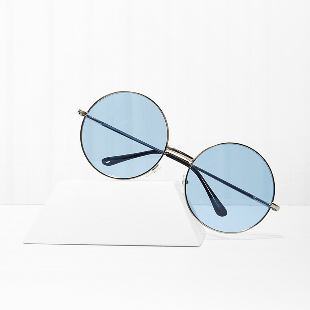 Round sunglasses with blue tinted lenses and thin metal frame on a white platform