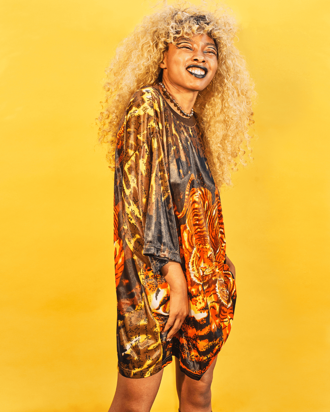 Woman wearing loose tiger print t-shirt dress with long sleeves against yellow background