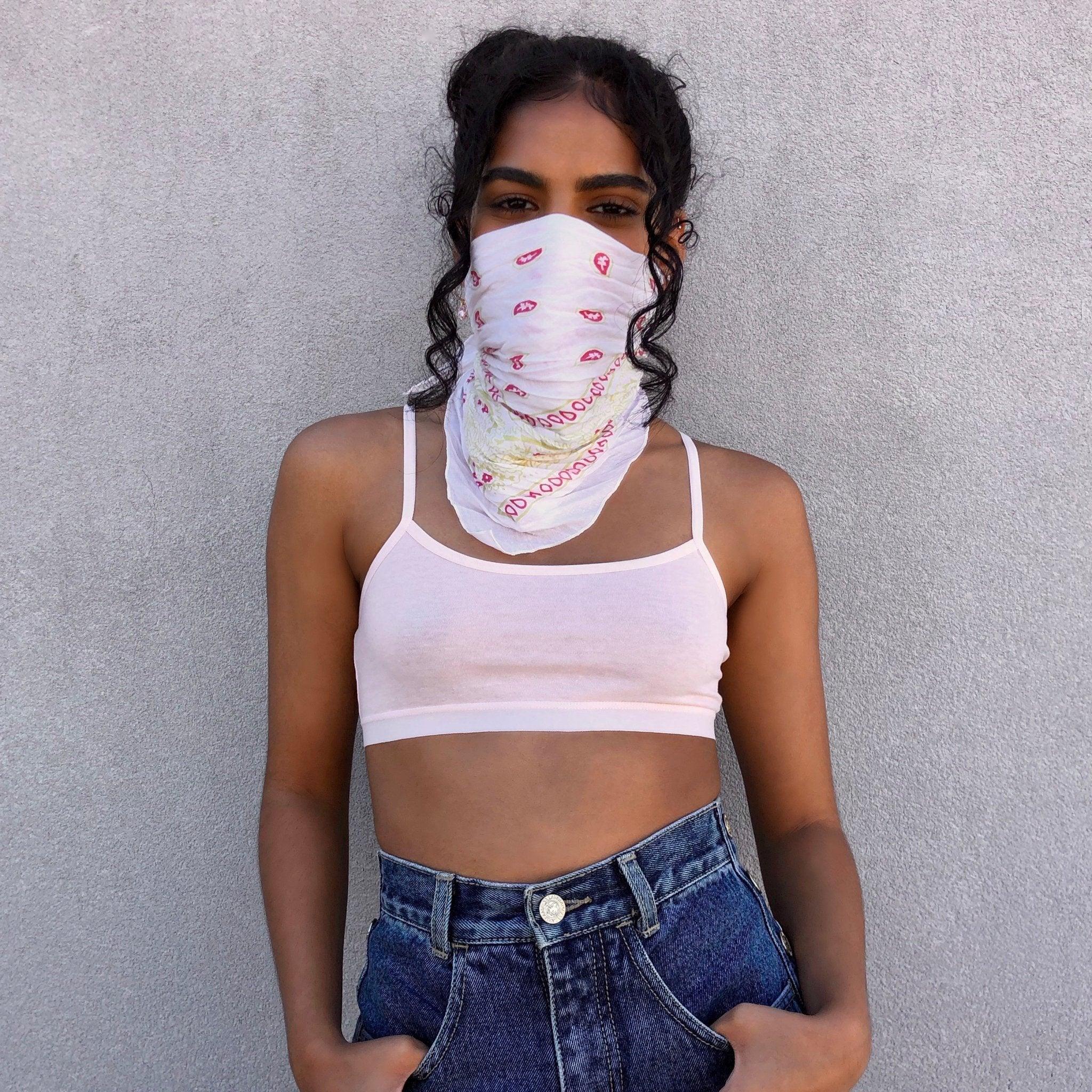 Woman wearing a white printed bandana and crop top, standing against a gray wall
