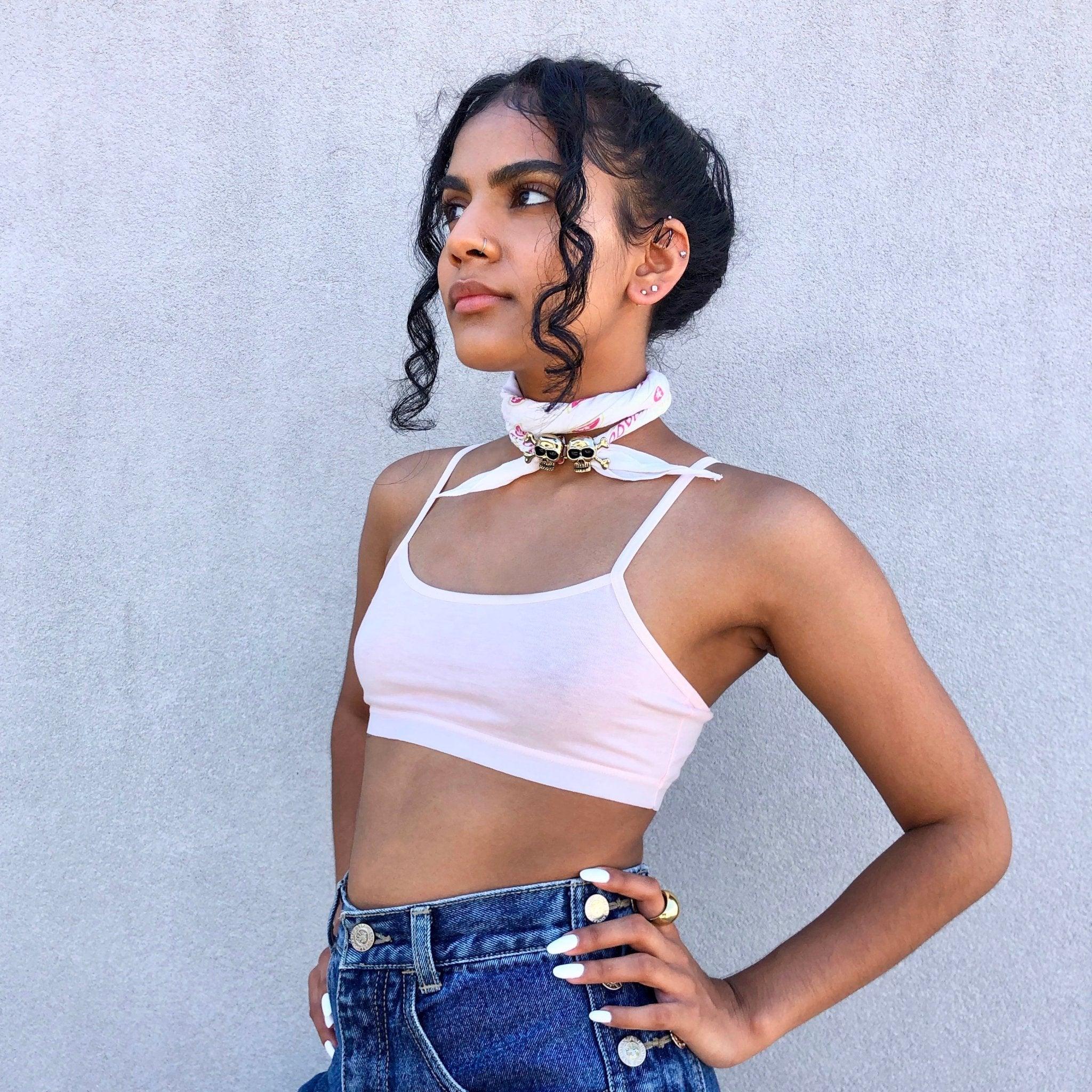 Woman wearing white crop top, blue jeans, and white bandana with metallic skulls