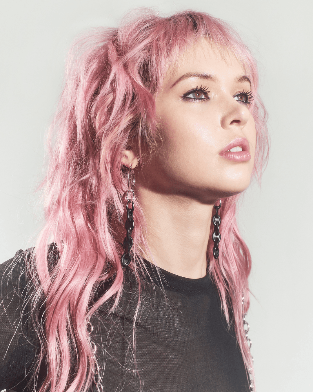 Woman with pink wavy hair wearing long black chain link earrings and a sheer black top