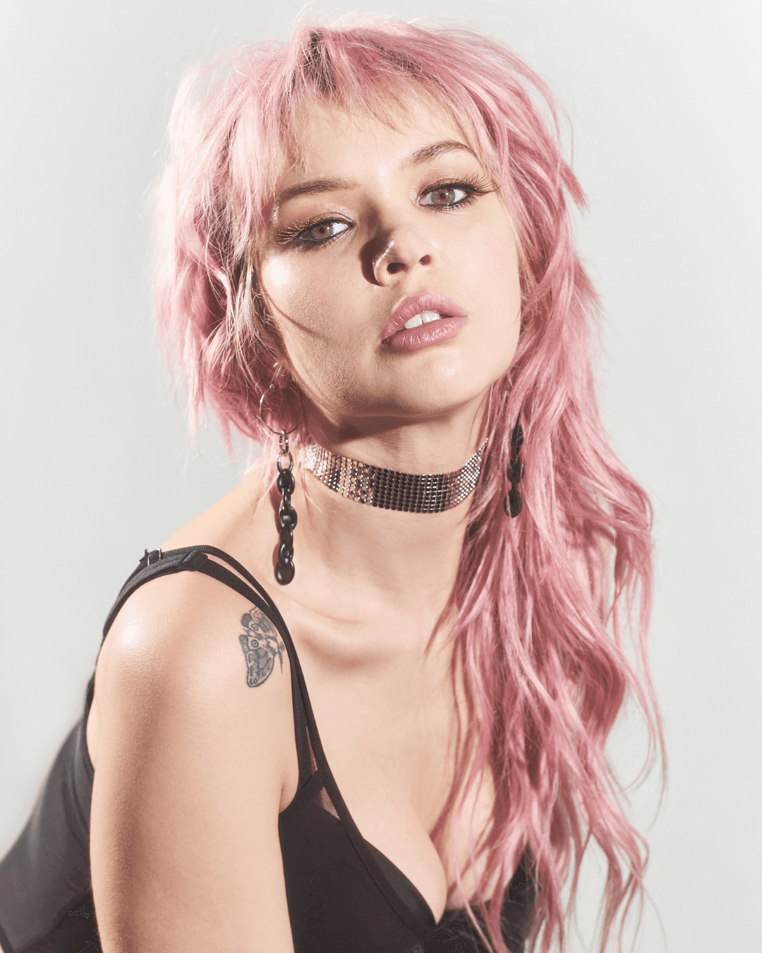 Woman with pink hair wearing a black top, silver choker, and black drop earrings
