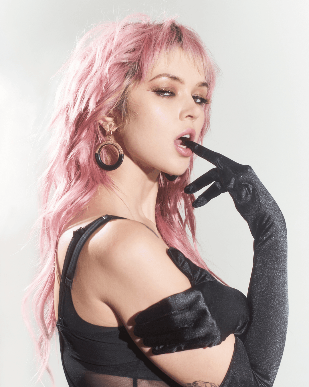 Woman with pink hair wearing gold and black hoop earrings and black satin gloves