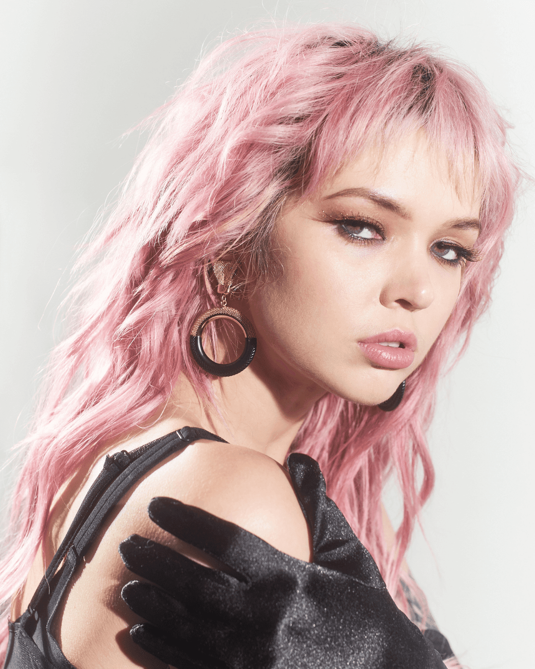 Woman with pink hair wearing black hoop earrings and a black glove on her shoulder