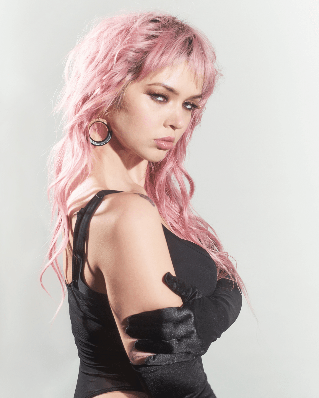 woman with pink hair wearing black hoop earrings, black outfit, and long black gloves