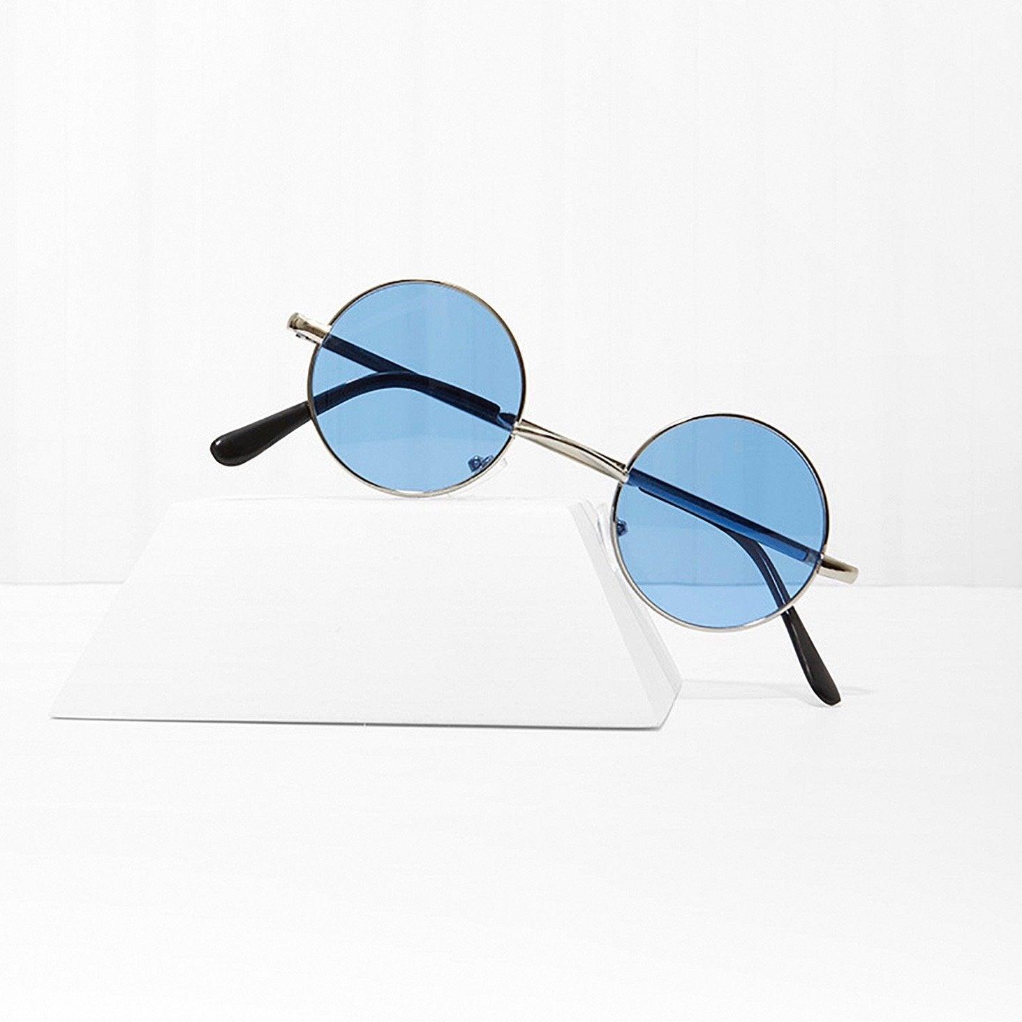 Round sunglasses with blue lenses and silver metal frame on white geometric stand