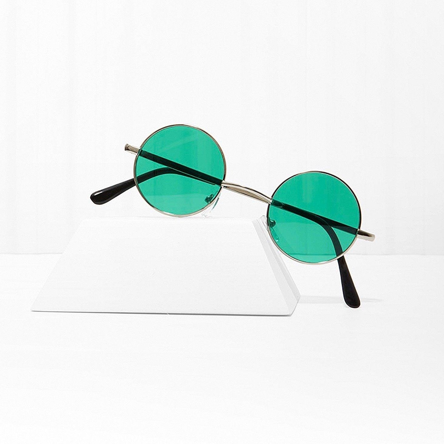 Round sunglasses with green lenses and thin metal frame on a white surface