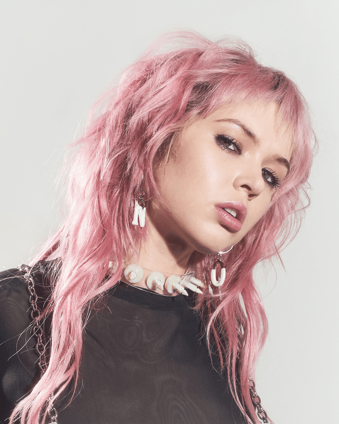 Person with pink hair wearing clear acrylic earrings shaped like letters and a chunky letter necklace