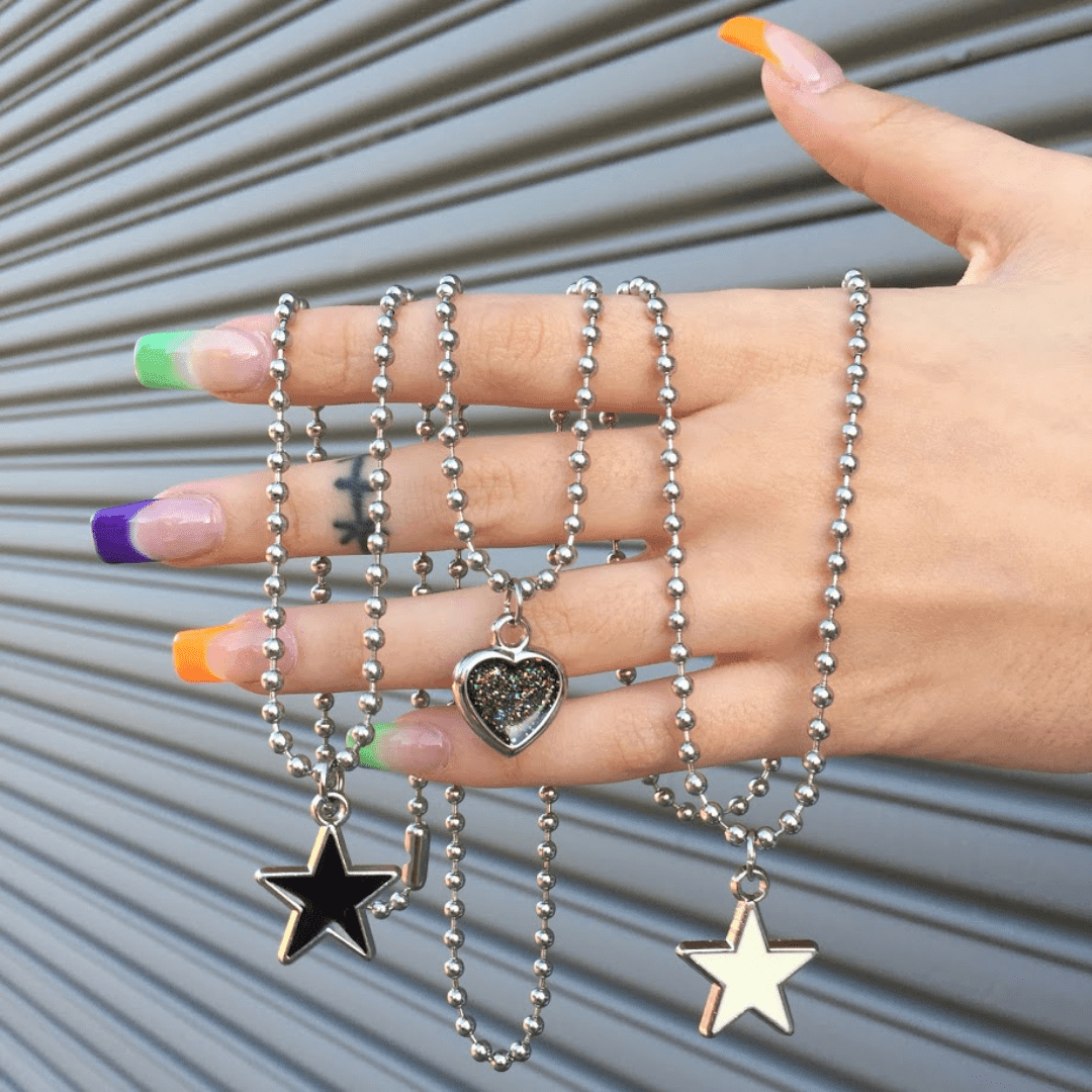 Hand with colorful nails holding silver ball chain necklaces with star and heart pendants
