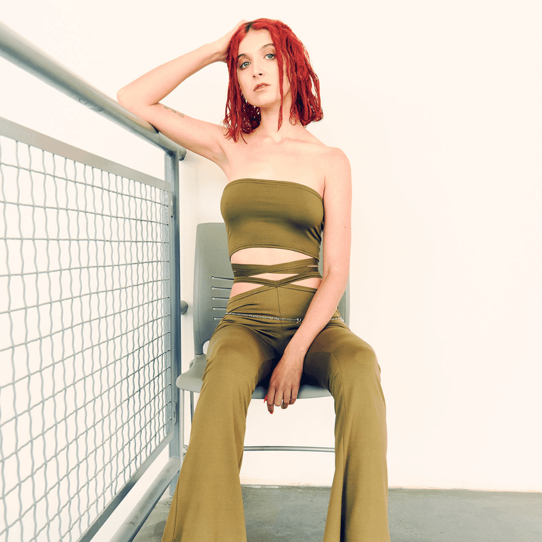 Woman in olive green strap tube top and matching flared pants sitting on a chair indoors
