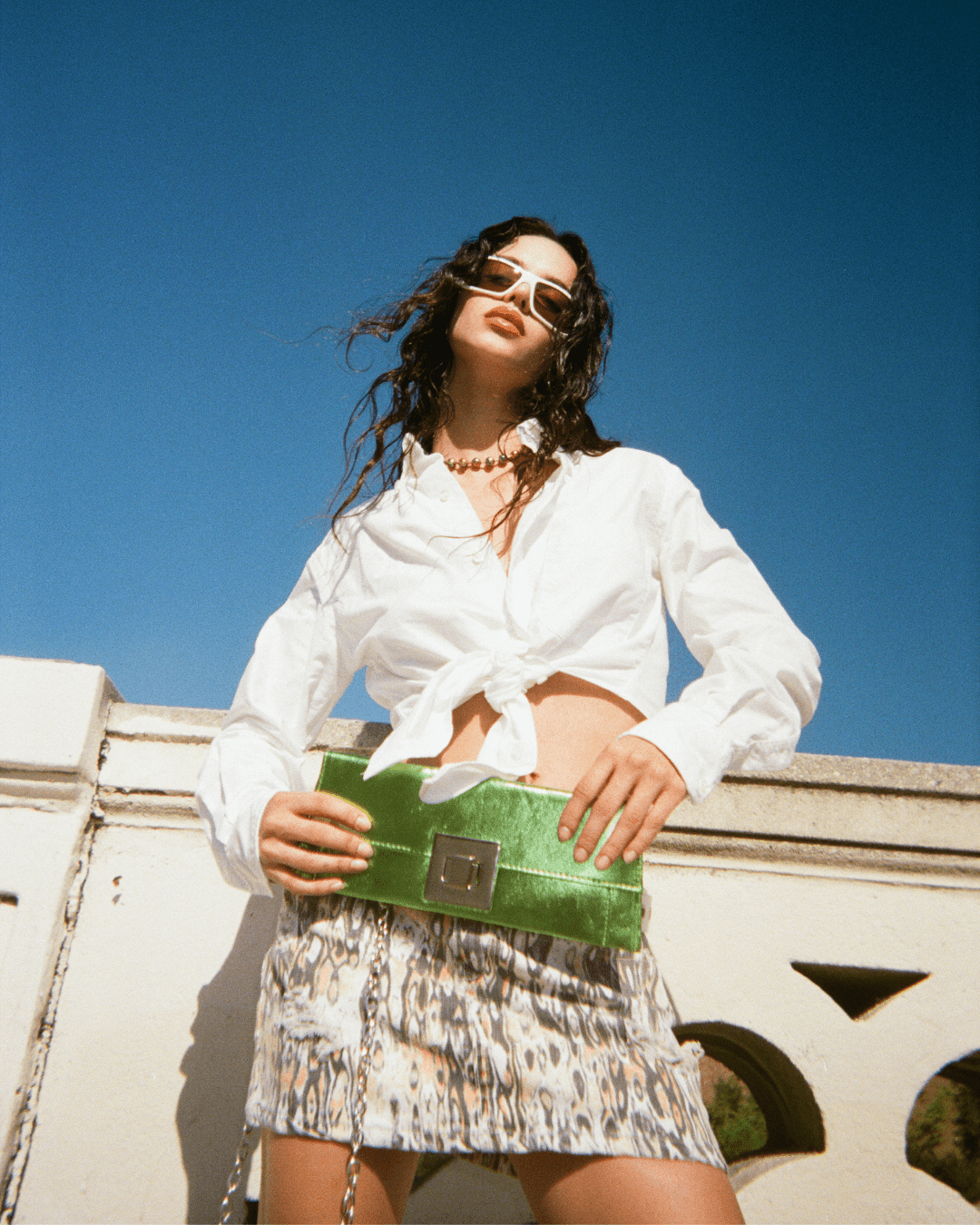Woman wearing animal print mini skirt, white tie-front shirt, holding green clutch outdoors