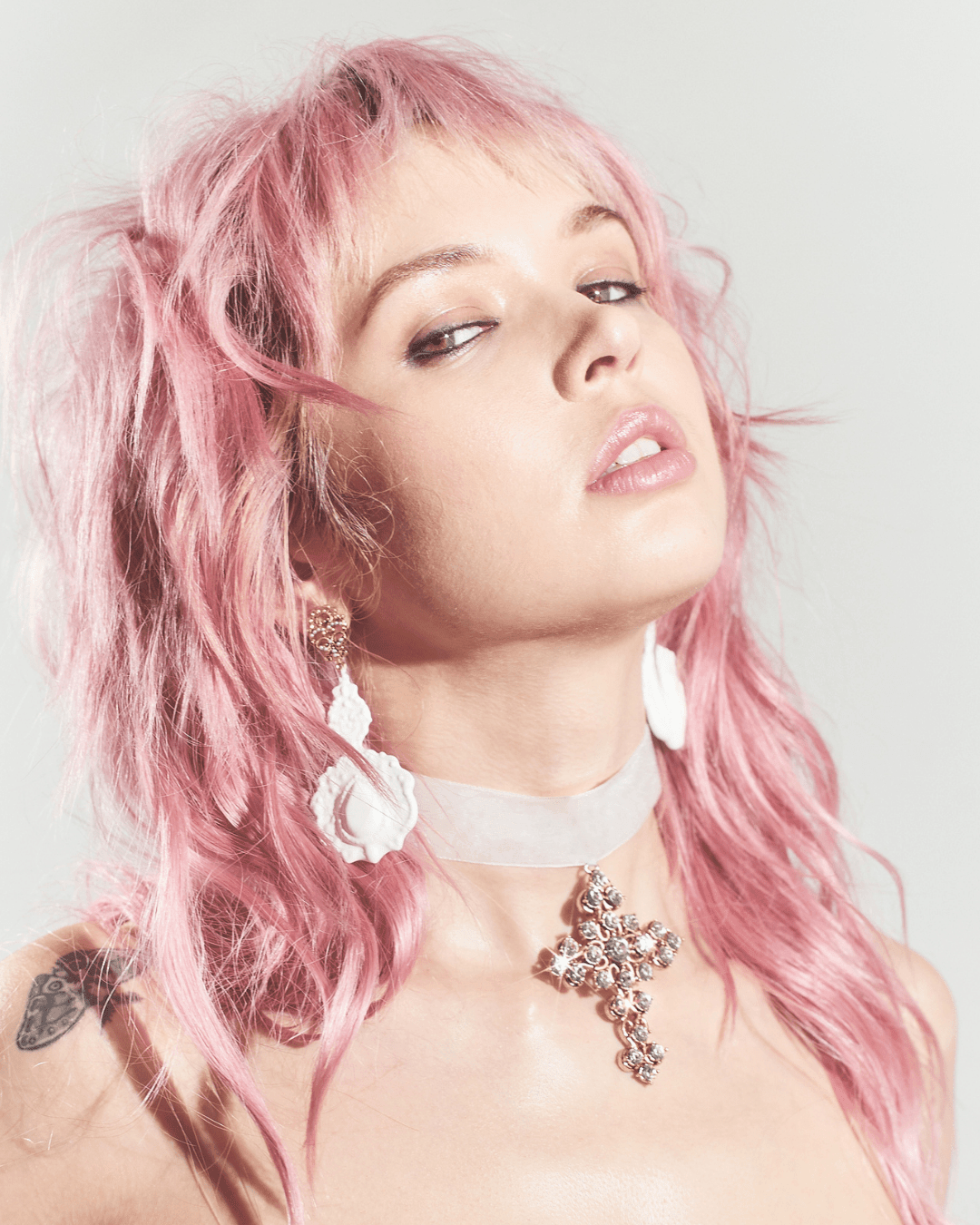 White drop earrings with a sculpted rose design on a person with pink hair