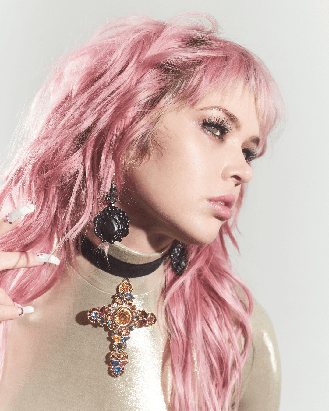 Large gold cross pendant with colorful gems and black lace earrings on a person