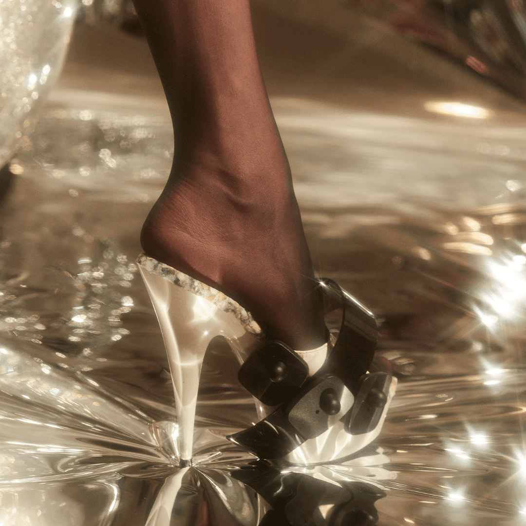 Clear platform heel with black bow details worn with black stockings on a shiny surface