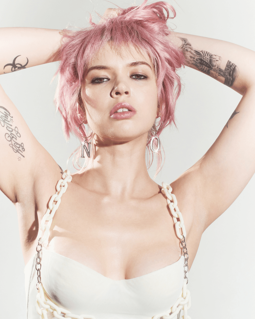 Silver letter earrings spelling NO, worn by a woman with pink hair and a white chain strap top