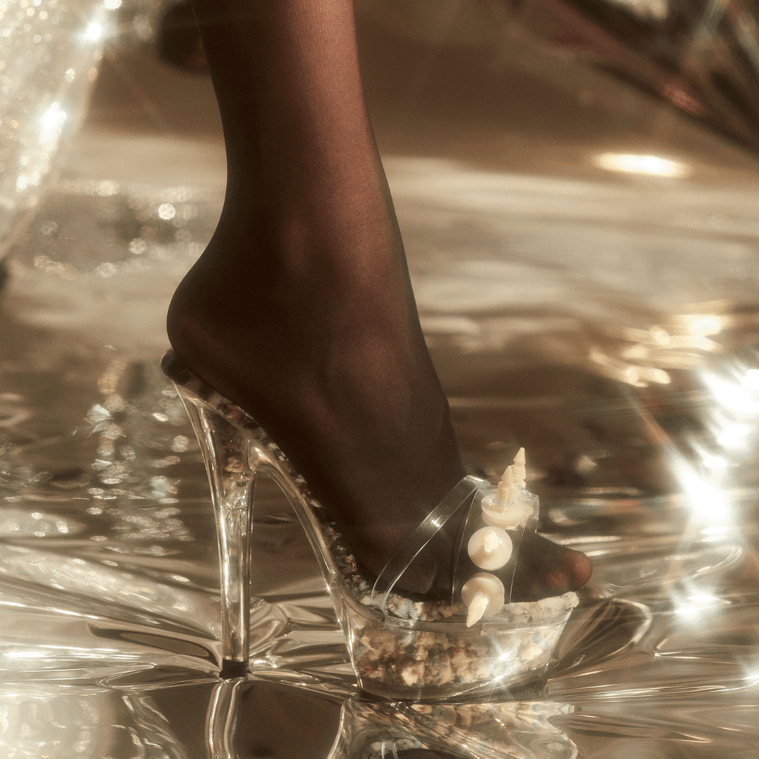 Clear platform high heel shoe with seashell accents, worn with black sheer tights