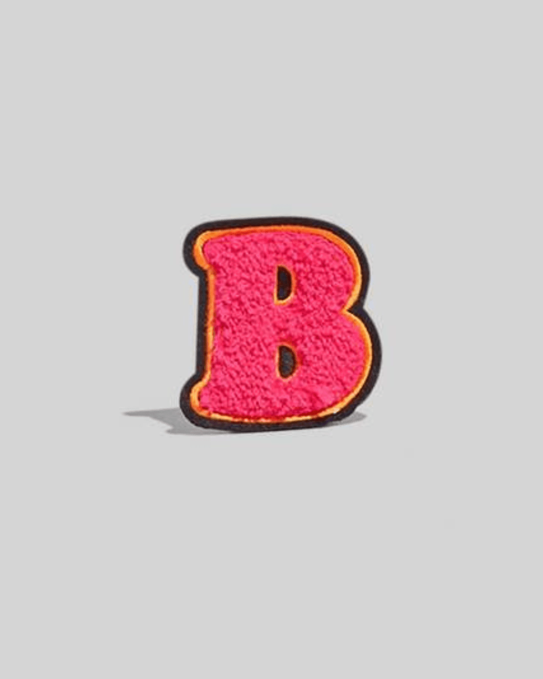 Pink chenille letter B patch with black and yellow border on a gray background