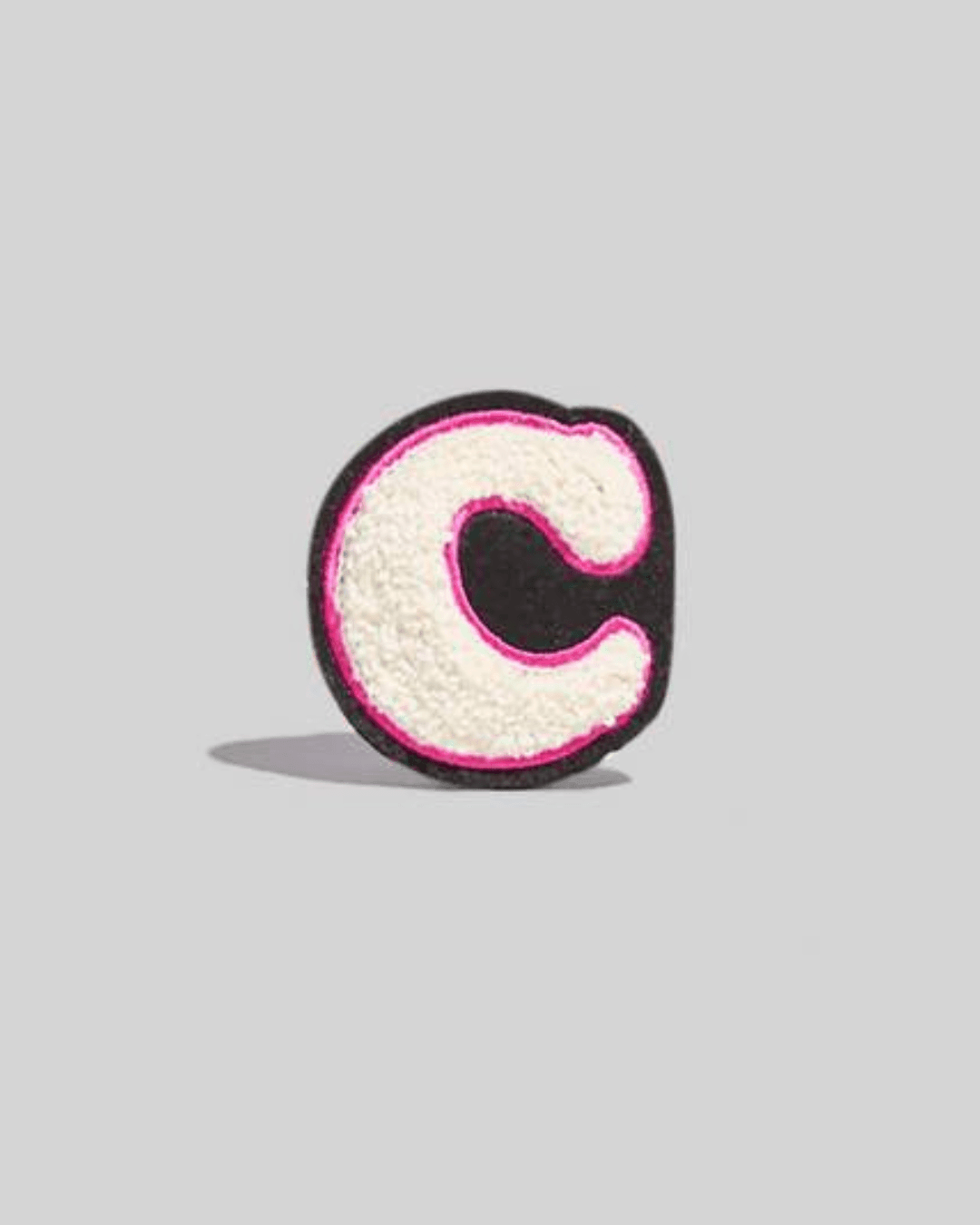 off-white chenille letter C patch with pink outline on a gray background