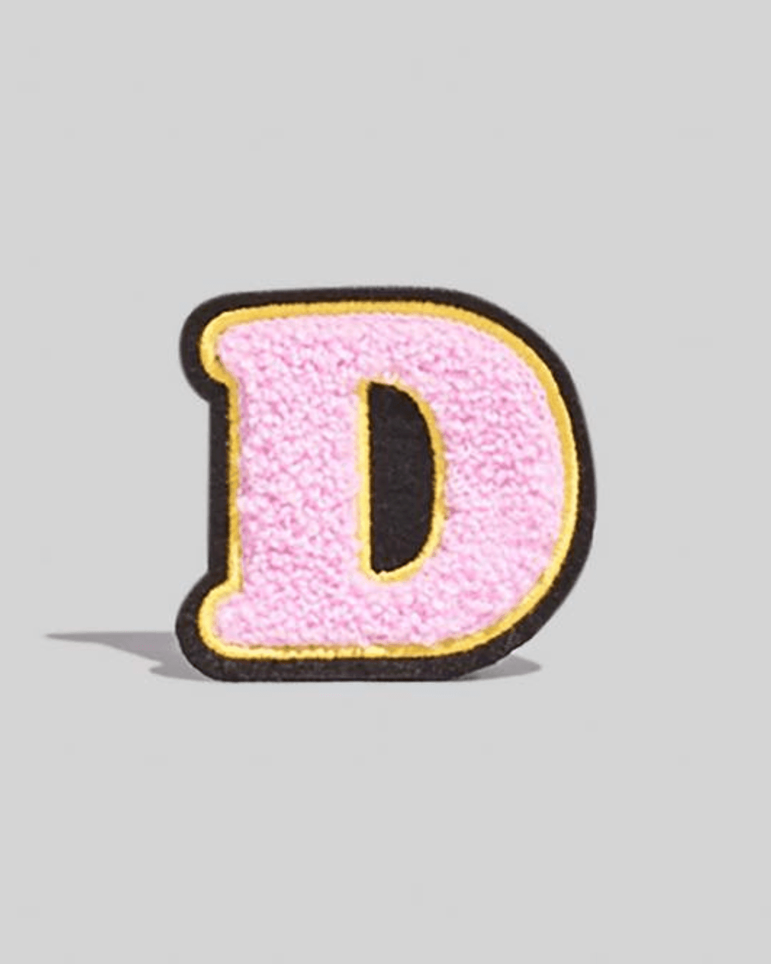 Large pink chenille varsity letter D patch with yellow and black border on a grey background