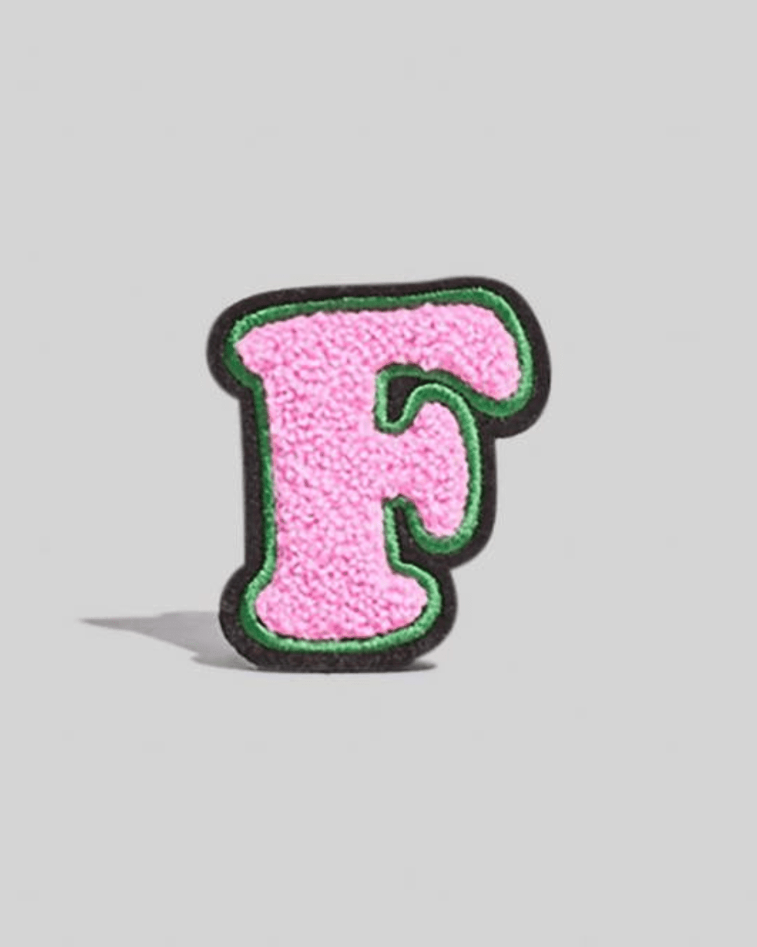 Pink chenille varsity letter F patch with green and black border on plain background