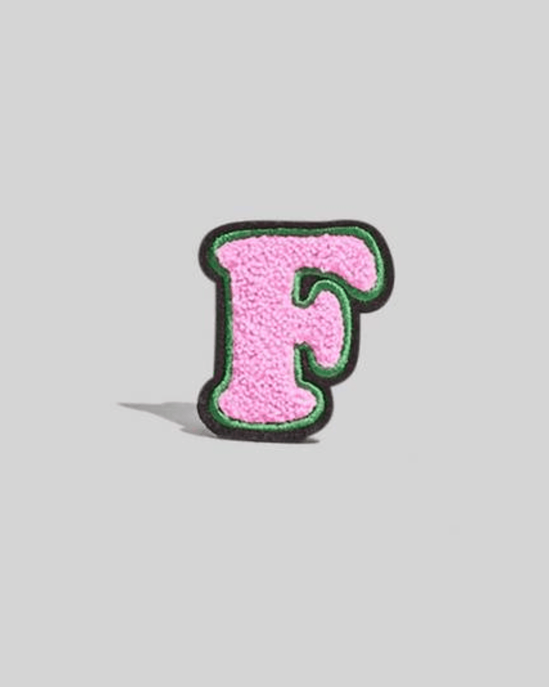 Pink chenille varsity letter F patch with green and black border on a gray background