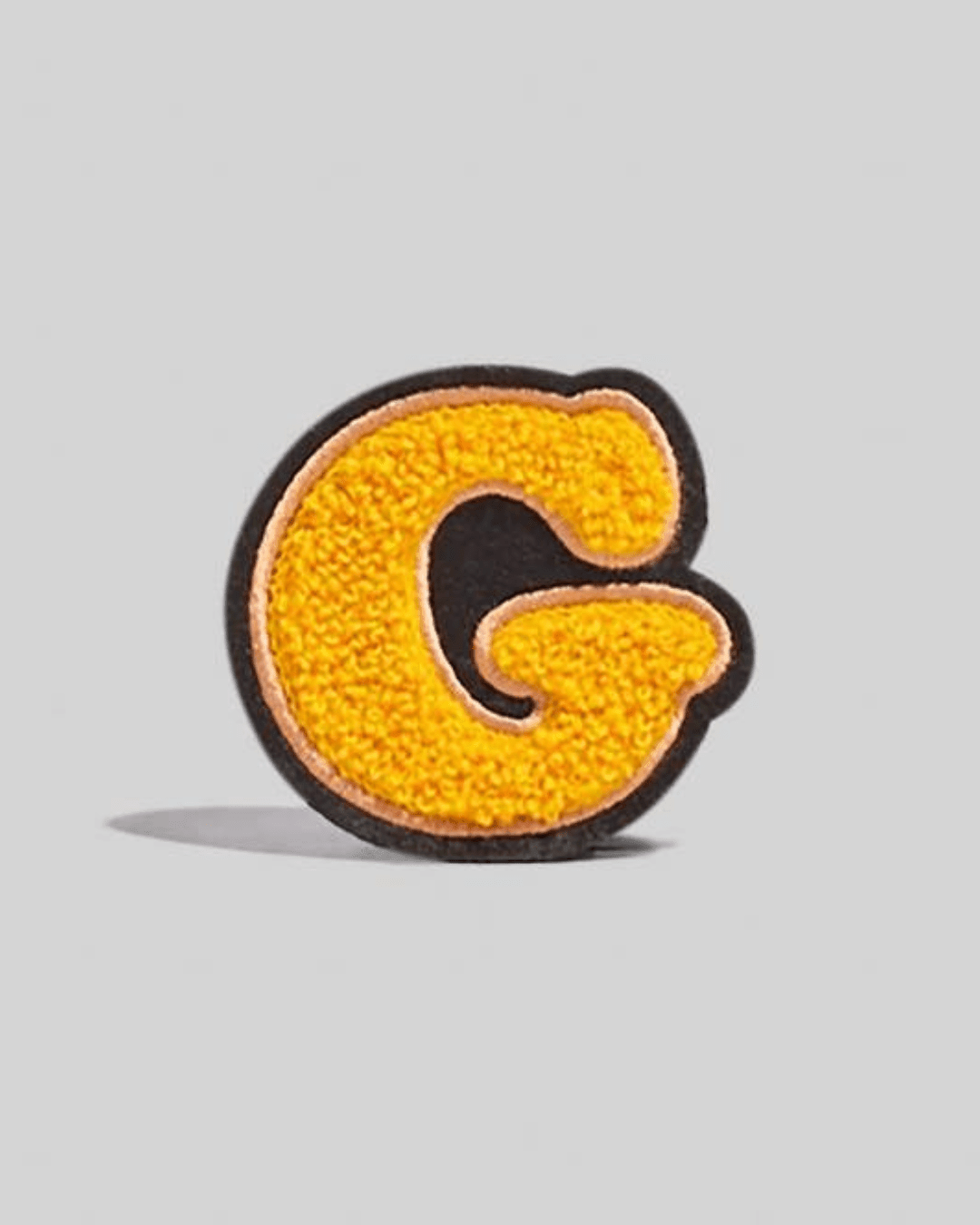 Yellow chenille varsity letter G patch with black and gold border on a gray background