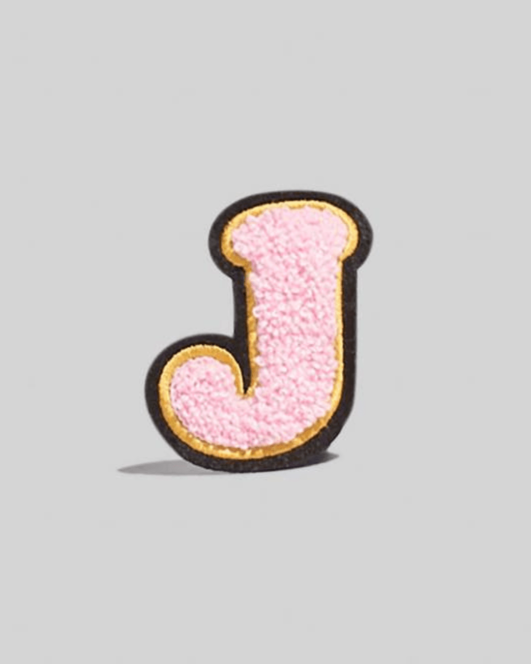 Large pink chenille letter J patch with gold and black border on gray background