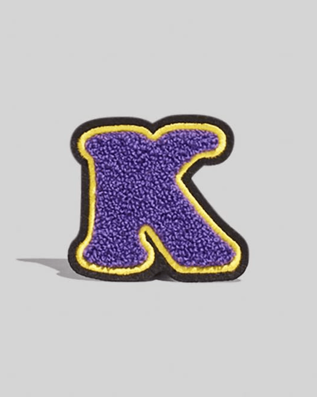 Purple chenille varsity letter K patch with yellow and black border on a gray background.