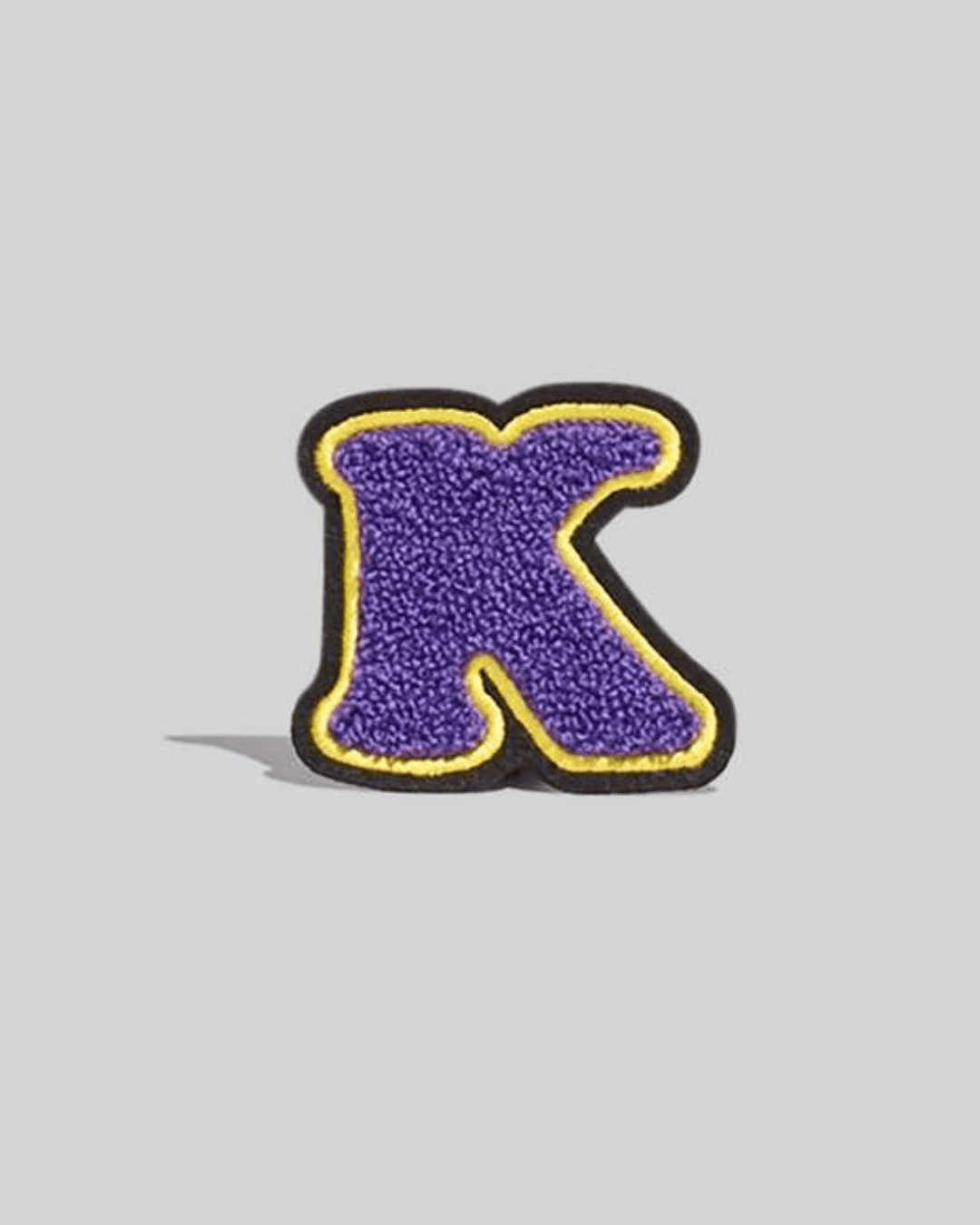 Purple chenille letter K varsity patch with yellow and black border on gray background