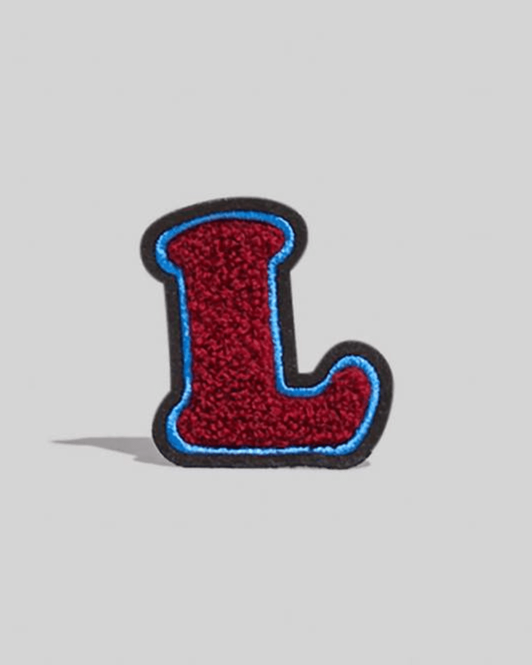 Large dark maroon chenille varsity letter L patch with blue and black border on gray background