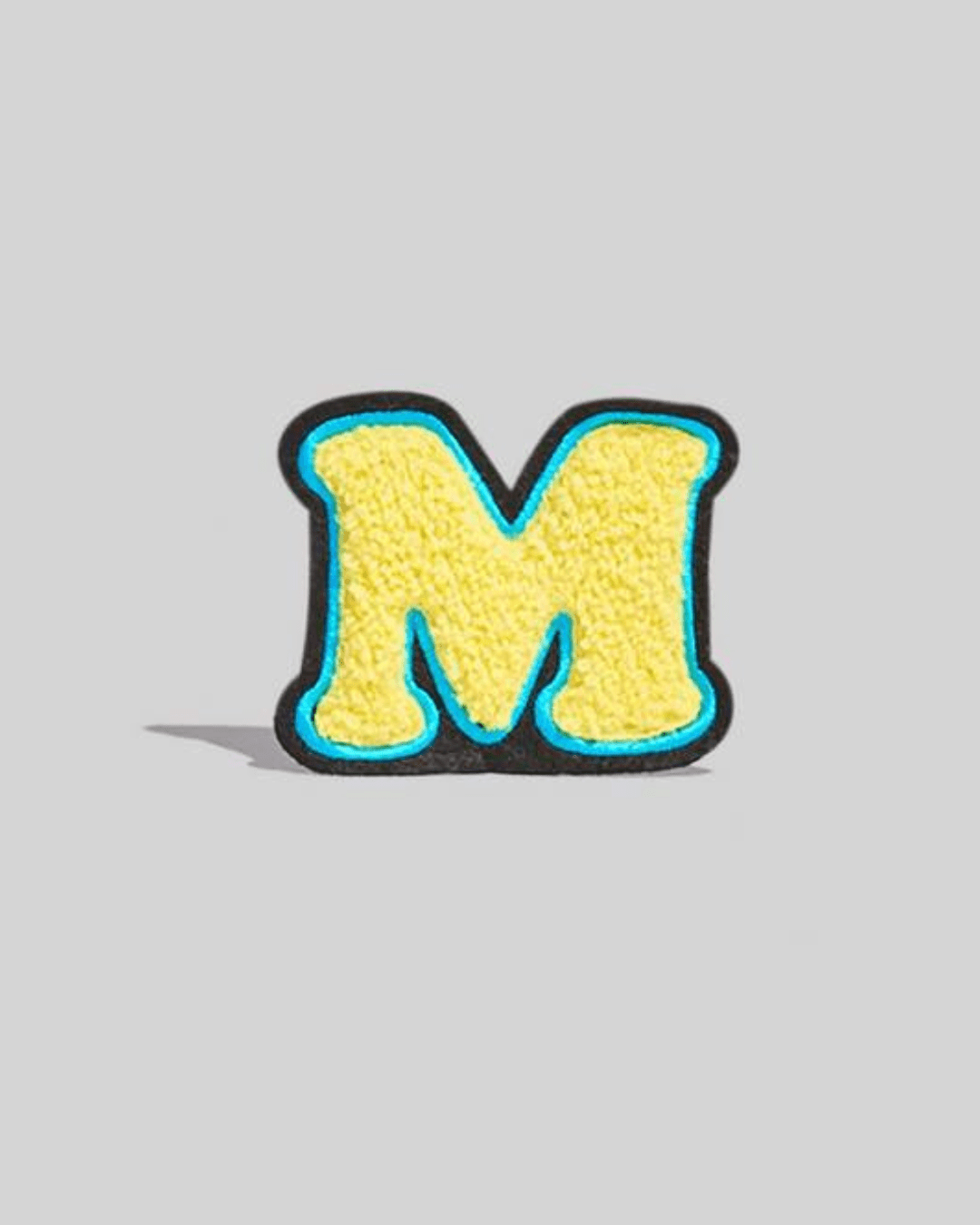 Yellow chenille letter M varsity patch with blue and black border on gray background