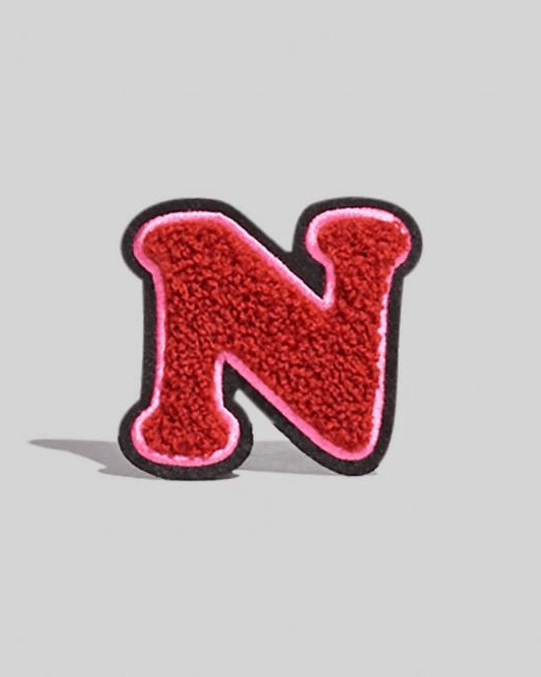Large maroon chenille varsity letter N patch with pink and black border on gray background