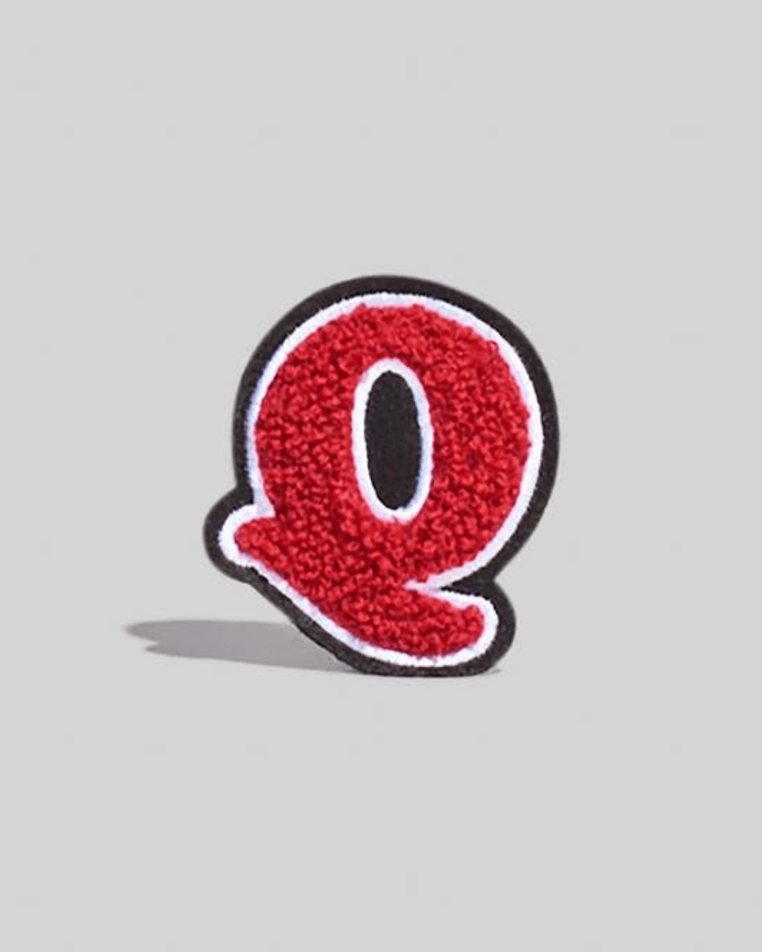 large red chenille letter Q varsity patch with black and white border on grey background