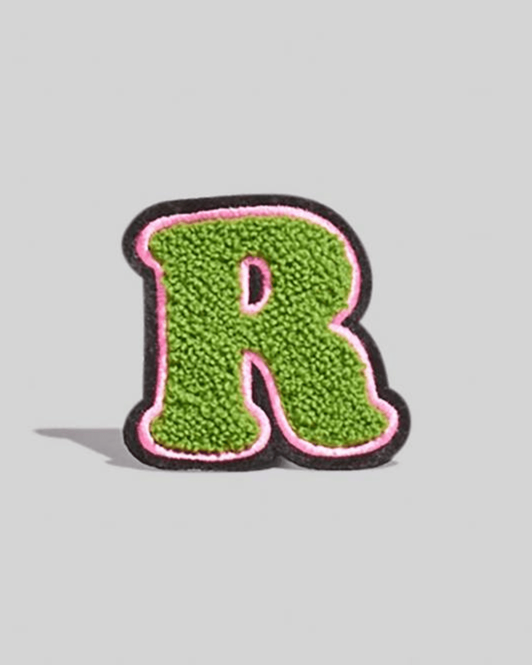 Large green chenille varsity letter R patch with pink and black border on gray background