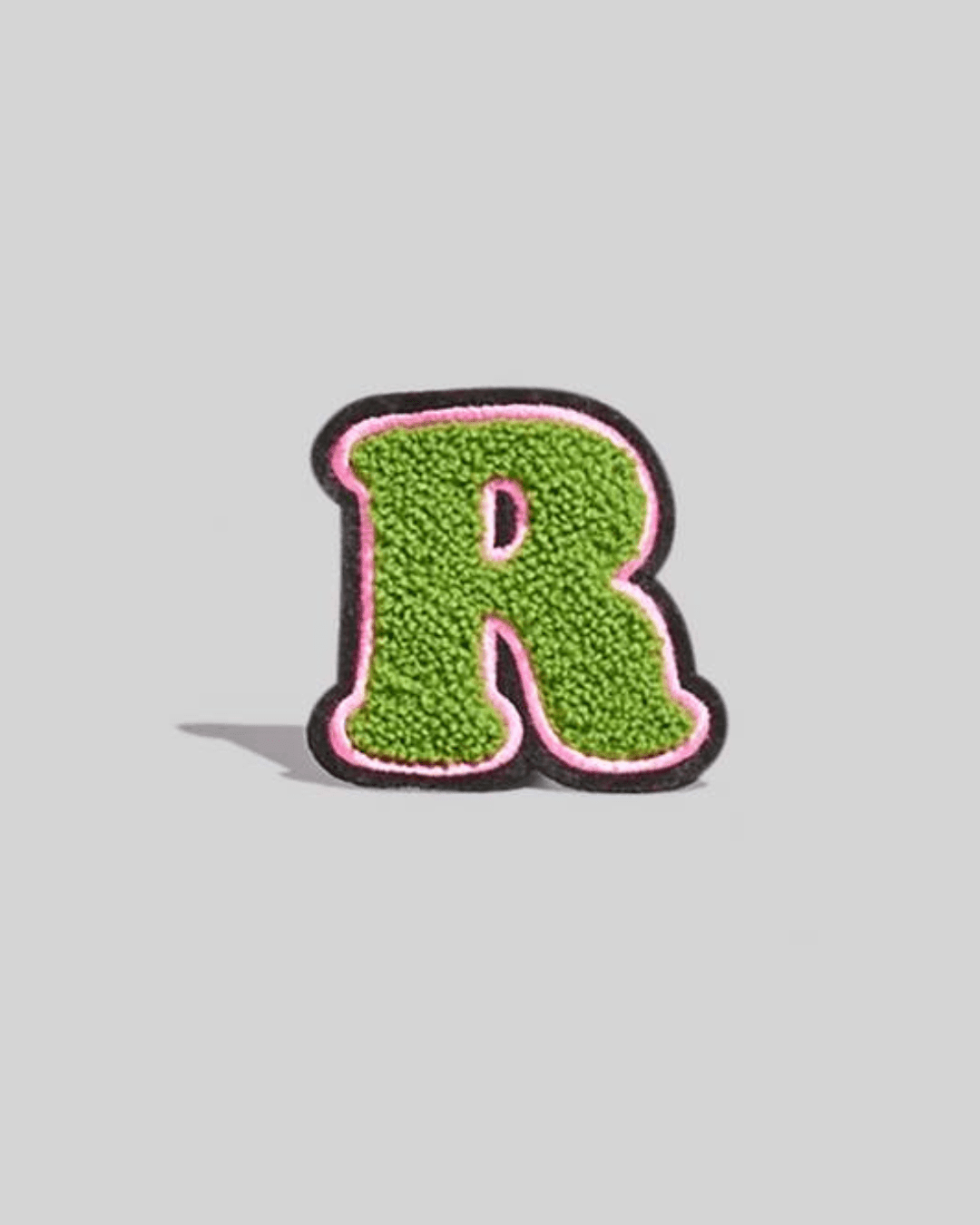 Green chenille varsity letter R patch with pink and black border on a gray background.