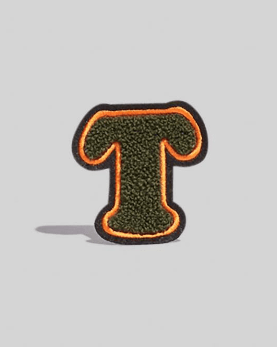 Large chenille varsity letter patch in olive green with orange border on gray background