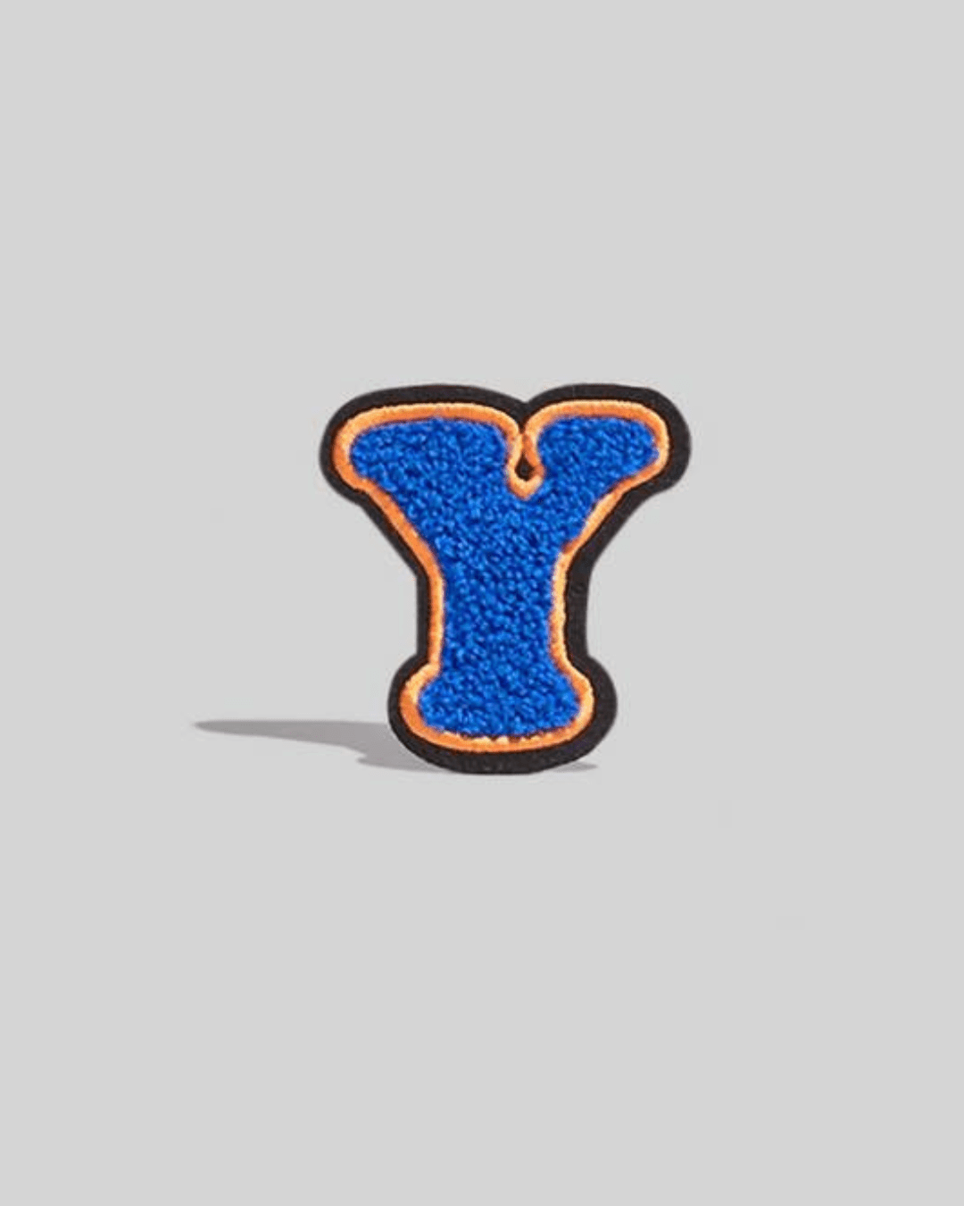 Small blue chenille varsity letter Y patch with orange and black border on gray background.